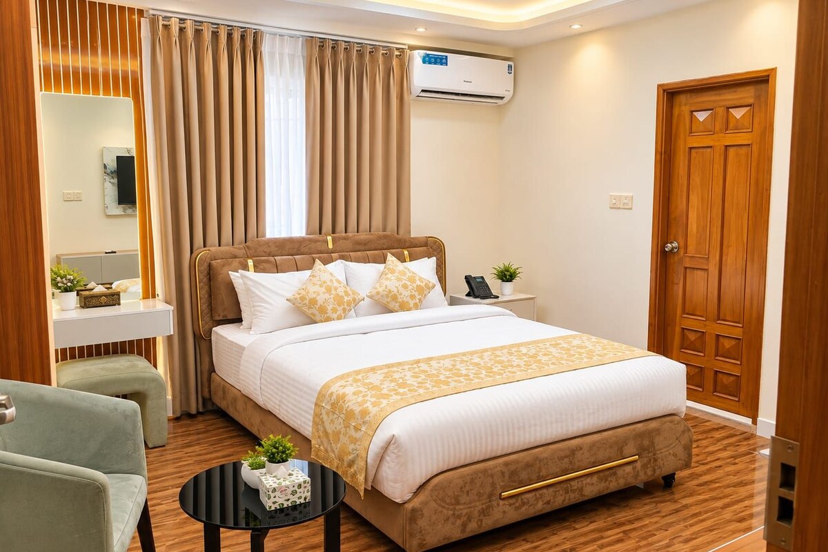 A hotel room with a bed, bedside table, chair, and a small round table with a plant.