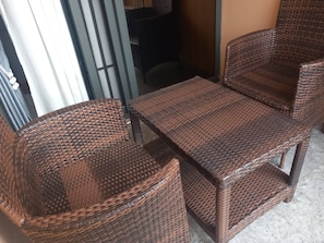Ein Korbmöbel-Set bestehend aus zwei Stühlen und einem Tisch, platziert in der Nähe einer Schiebetür aus Glas.