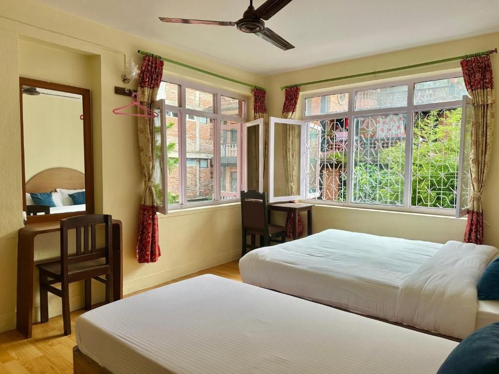 A bedroom with a bed, a desk, and a chair, with windows offering a view of greenery.