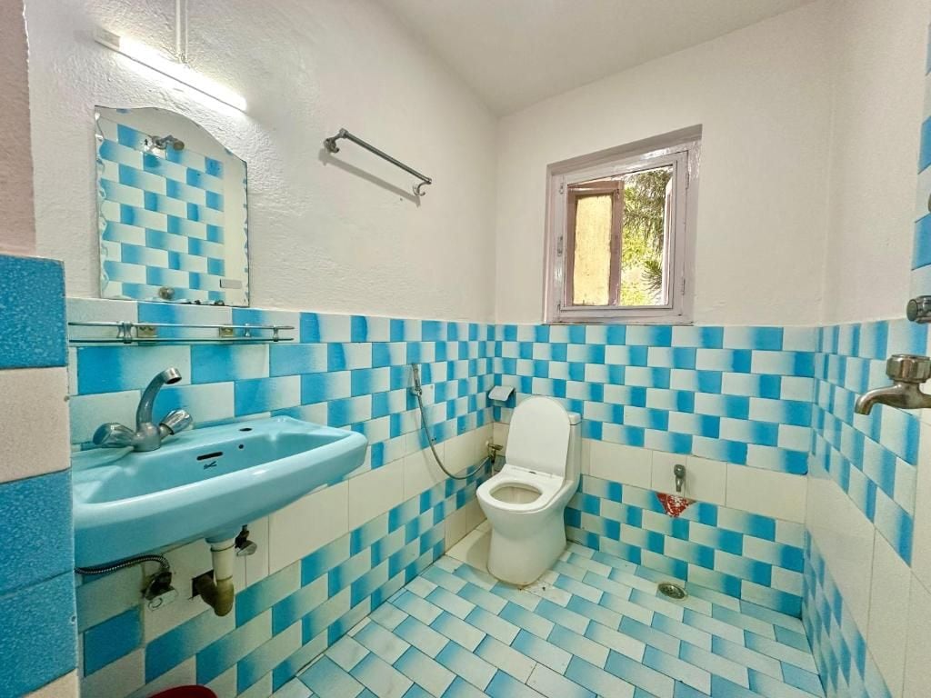 A bathroom with a checkered floor pattern, a sink, a toilet, and a window.