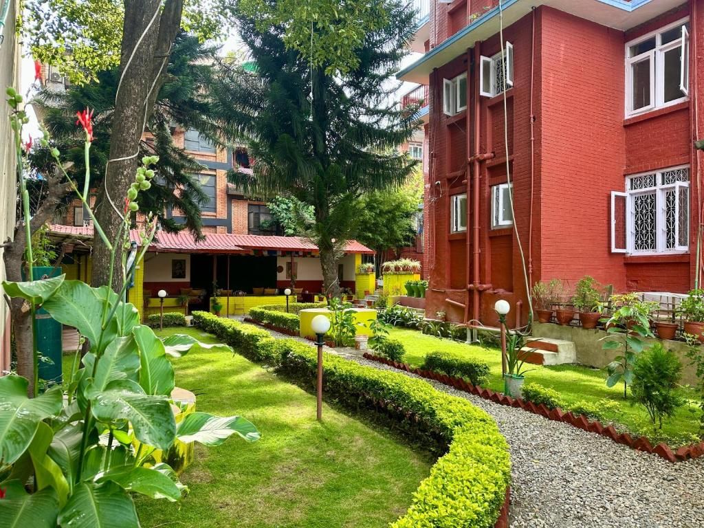 A courtyard with a red building, a pathway, and various plants.