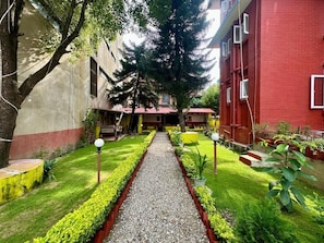 A courtyard with a gravel path, green hedges, and a red building. - My Garden house (Kathmandu)