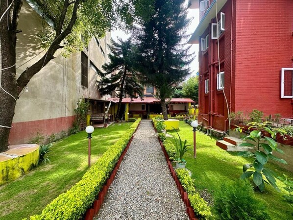 A courtyard with a gravel path, green hedges, and a red building.