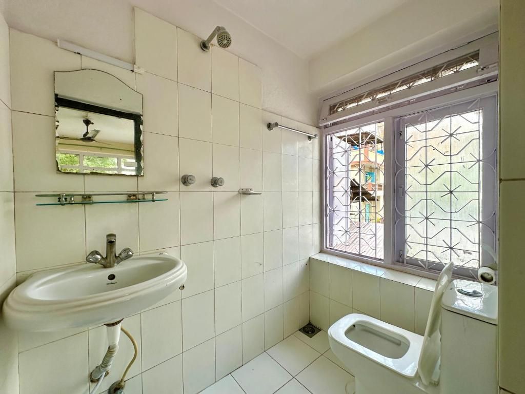 Une salle de bain avec un lavabo blanc, un miroir, une fenêtre avec une grille en métal et des toilettes.