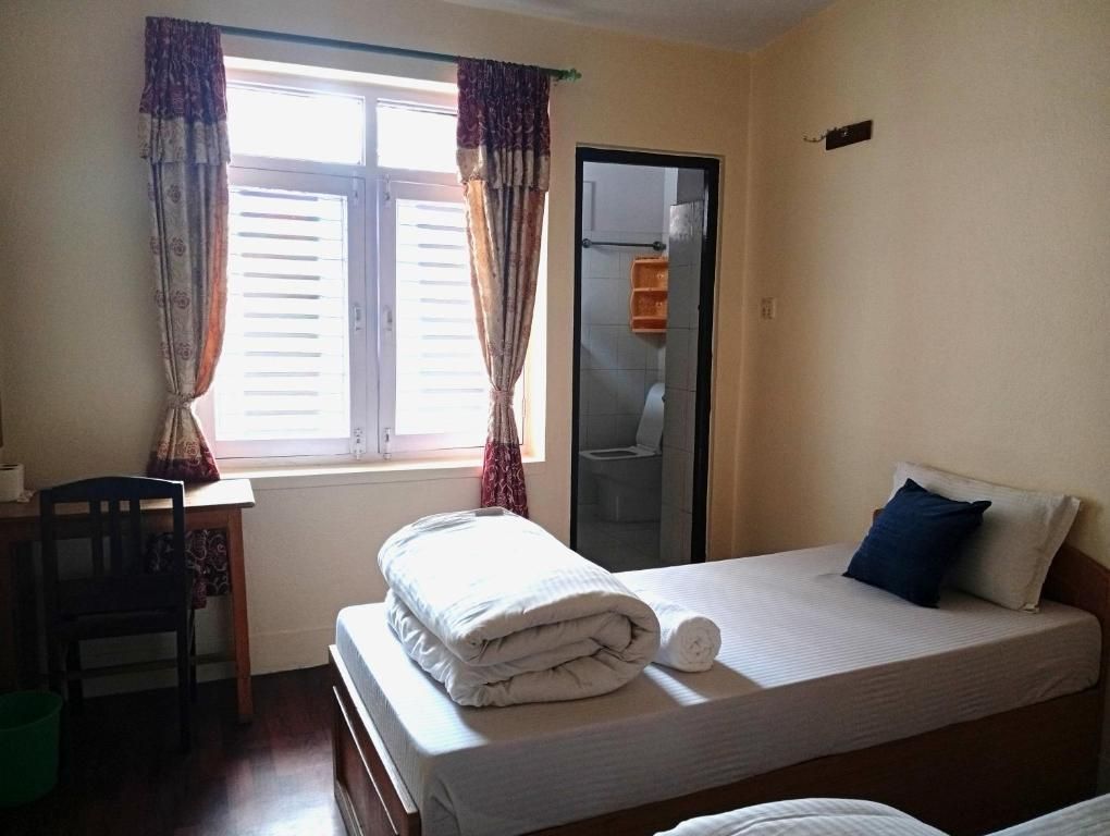 A single bed with a rolled-up towel, a chair, a small table, and a window with curtains.