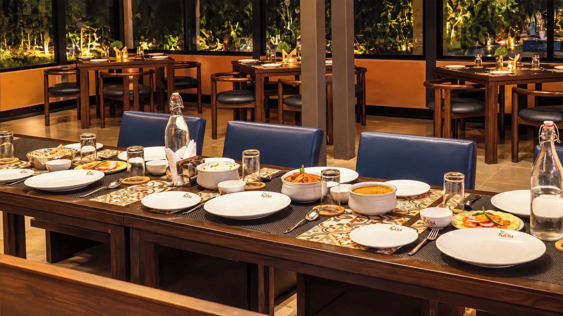 A restaurant dining area with multiple tables set for meals, chairs, and a view of greenery outside.
