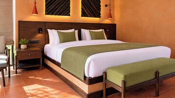 A neatly made bed with a green throw, a wooden nightstand with a plant, and a wall-mounted light fixture.