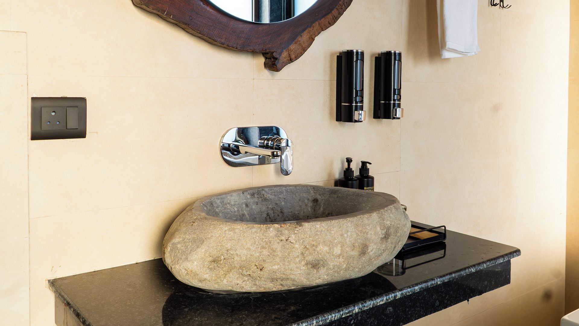 A bathroom with a stone sink, a chrome faucet, and two black bottles on the wall.