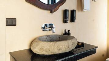 A bathroom with a stone sink, a chrome faucet, and two black bottles on the wall.
