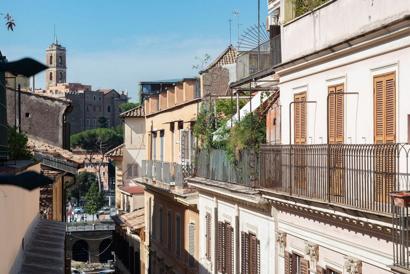A narrow street with historic buildings, a bell tower, and a pedestrian bridge.