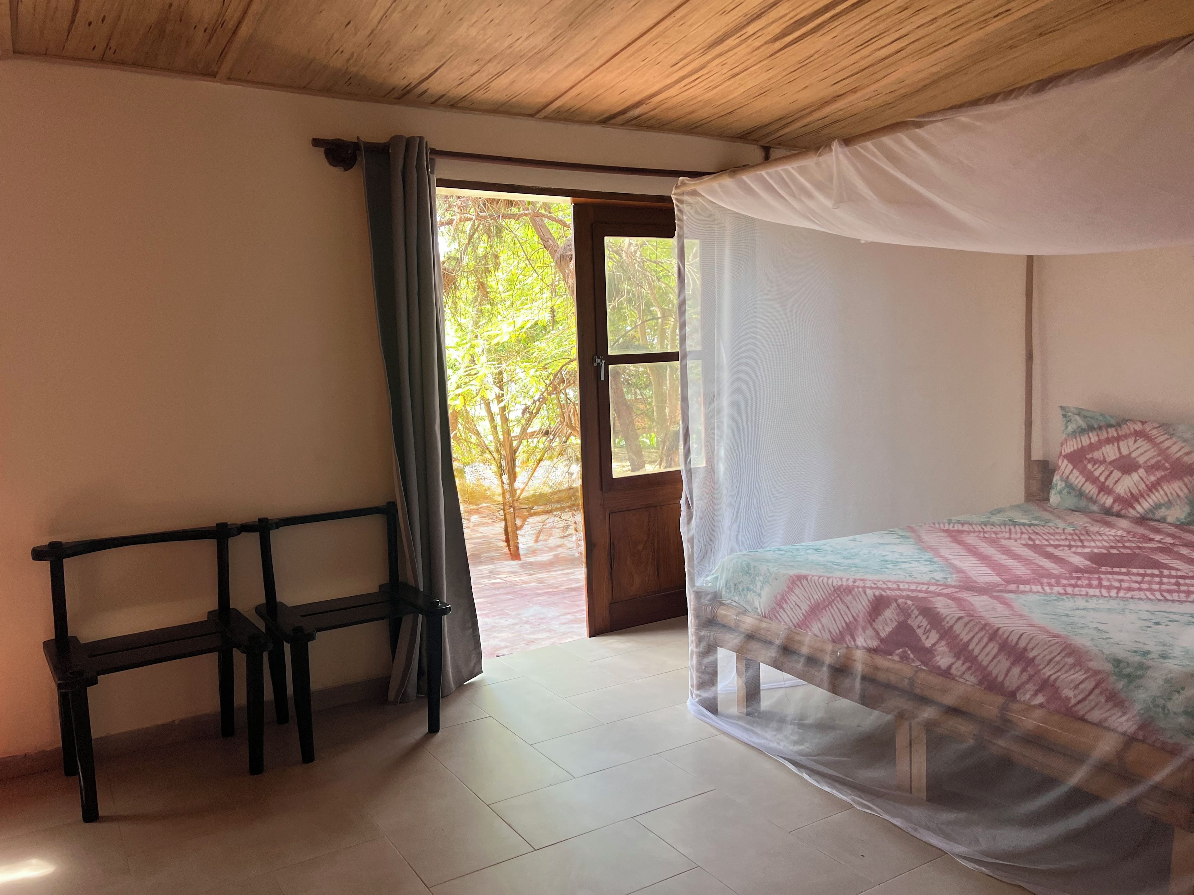 Una habitación con una cama, un banco y una puerta que da al exterior.