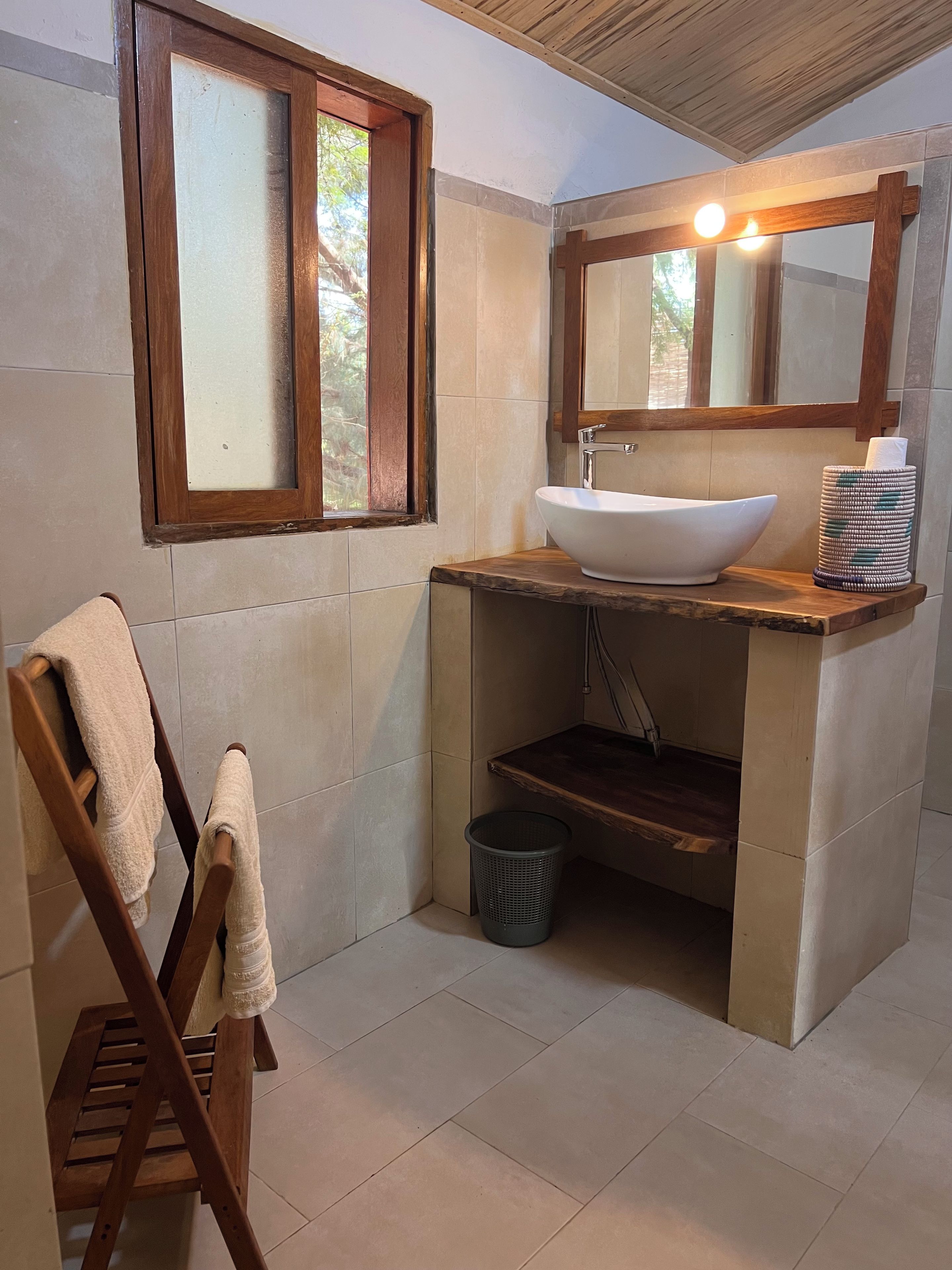 Un baño con ventana de madera, un lavamanos blanco y un perchero para toallas.