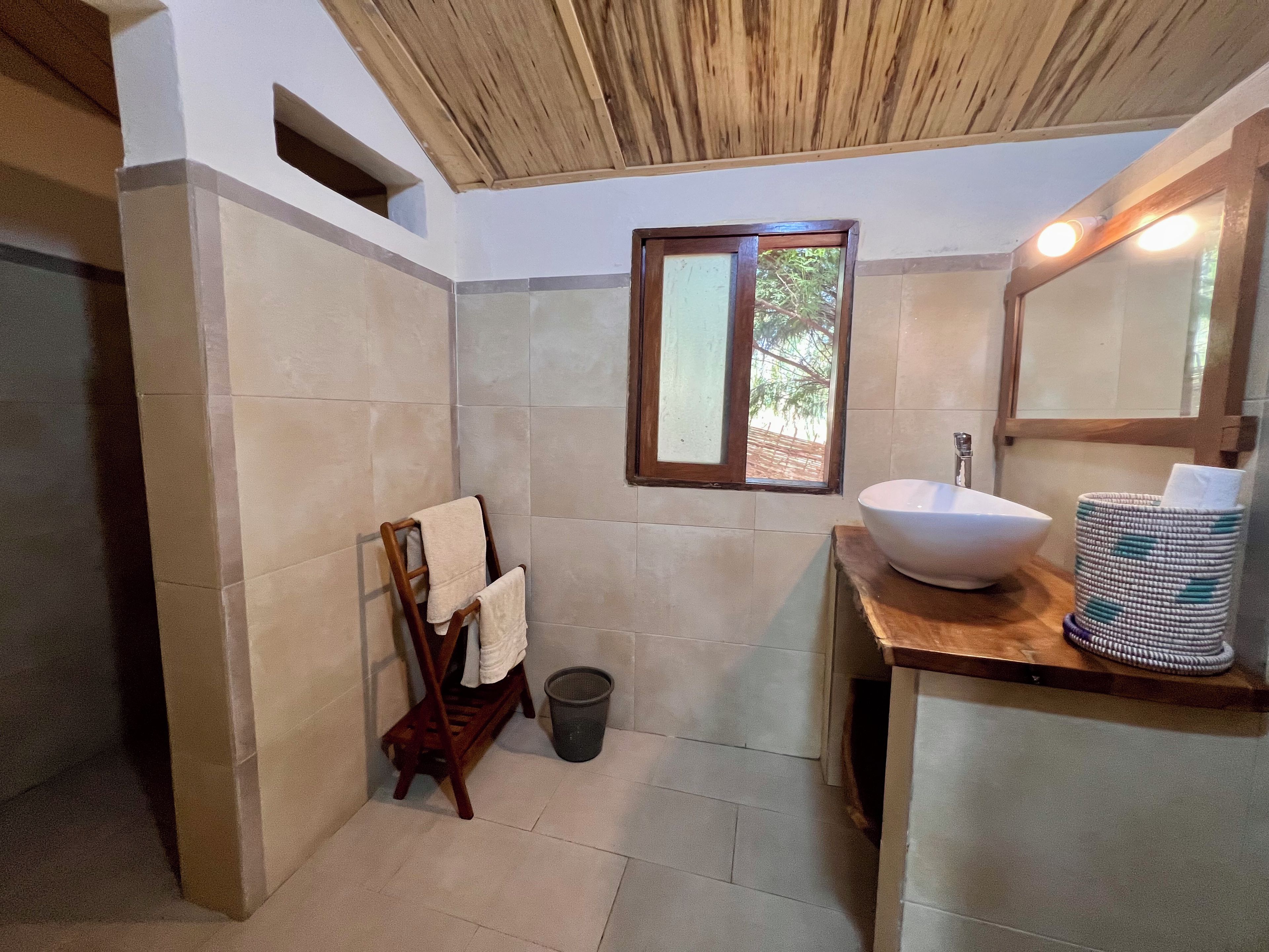 Un baño con un banco de madera, un lavabo, una ventana y un cubo de basura.