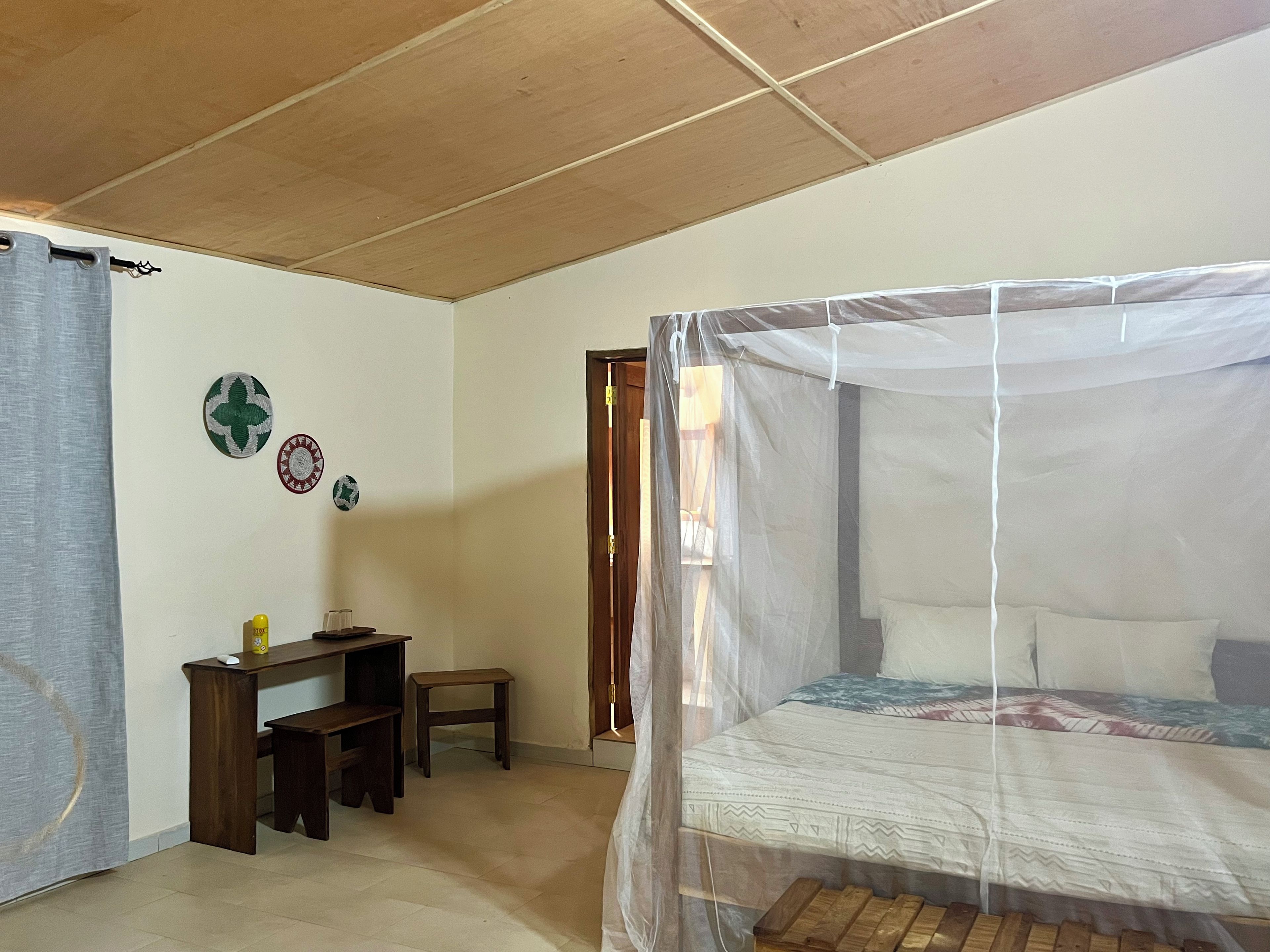 Un dormitorio con una cama bajo una mosquitera, un escritorio con una silla y un taburete pequeño.