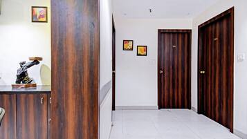Un pasillo con una puerta de madera, una pared blanca con dos cuadros enmarcados y una estatua sobre un mueble.