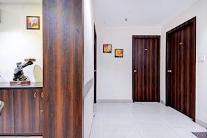 A hallway with a wooden door, a white wall with two framed pictures, and a statue on a cabinet. - Collection O Motisarai (Kolkata)