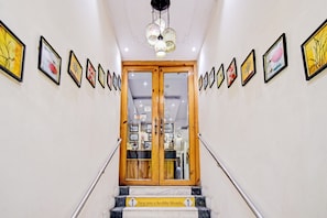 A staircase leading to a room with a wooden door, flanked by framed artwork on the walls. - Collection O Motisarai (Kolkata)