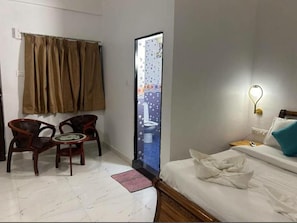 A hotel room with a bed, a bedside table, a lamp, a window with curtains, a small table with chairs, and a view of the bathroom. - Hotel Ashoka King (Ashvem)
