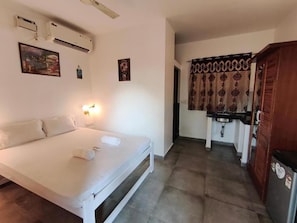 A bedroom with a bed, bedside table, and wall-mounted air conditioning unit. - Hotel Ashoka King (Ashvem)