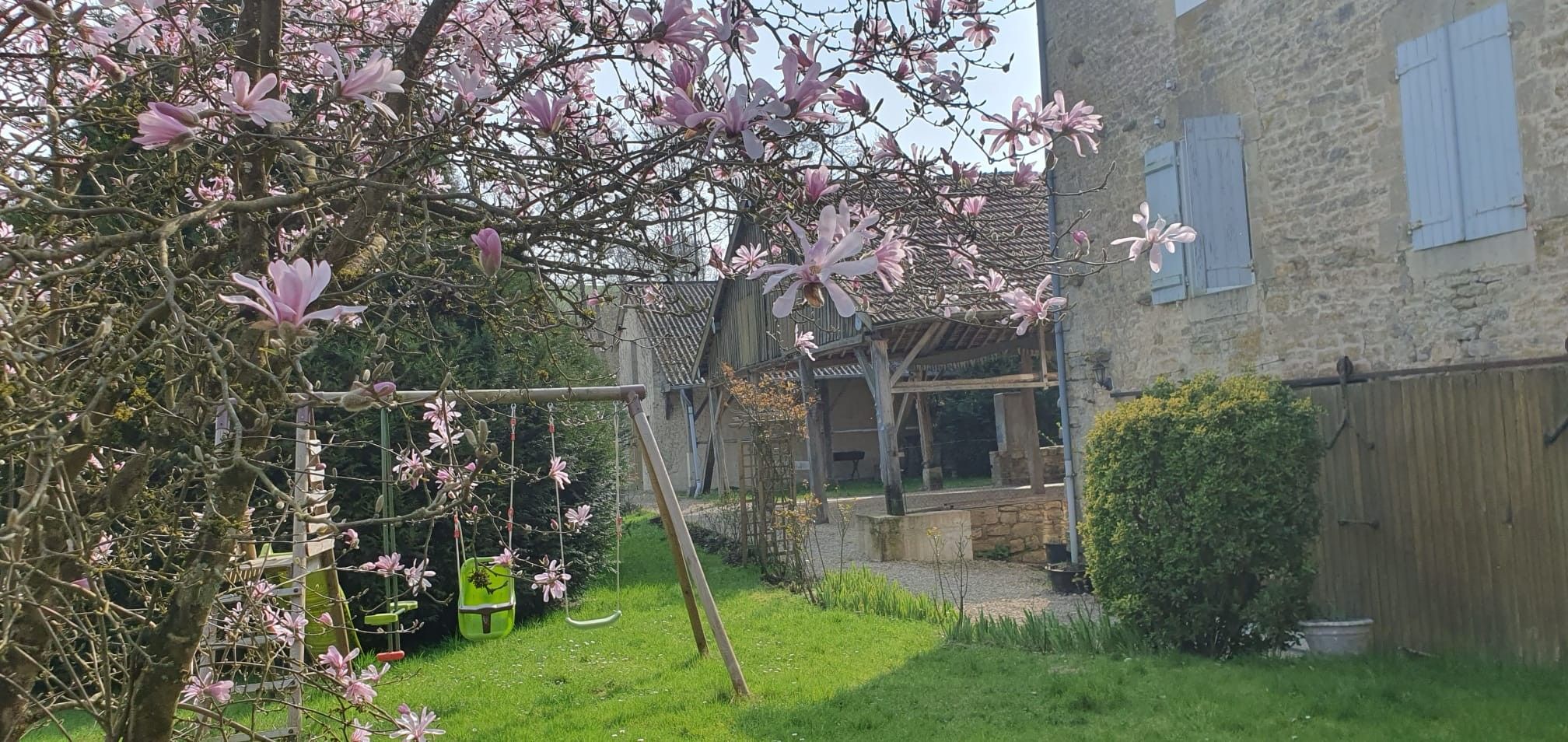 Ein Garten mit blühenden Bäumen, einer hölzernen Konstruktion und einem Gebäude mit Fenstern.