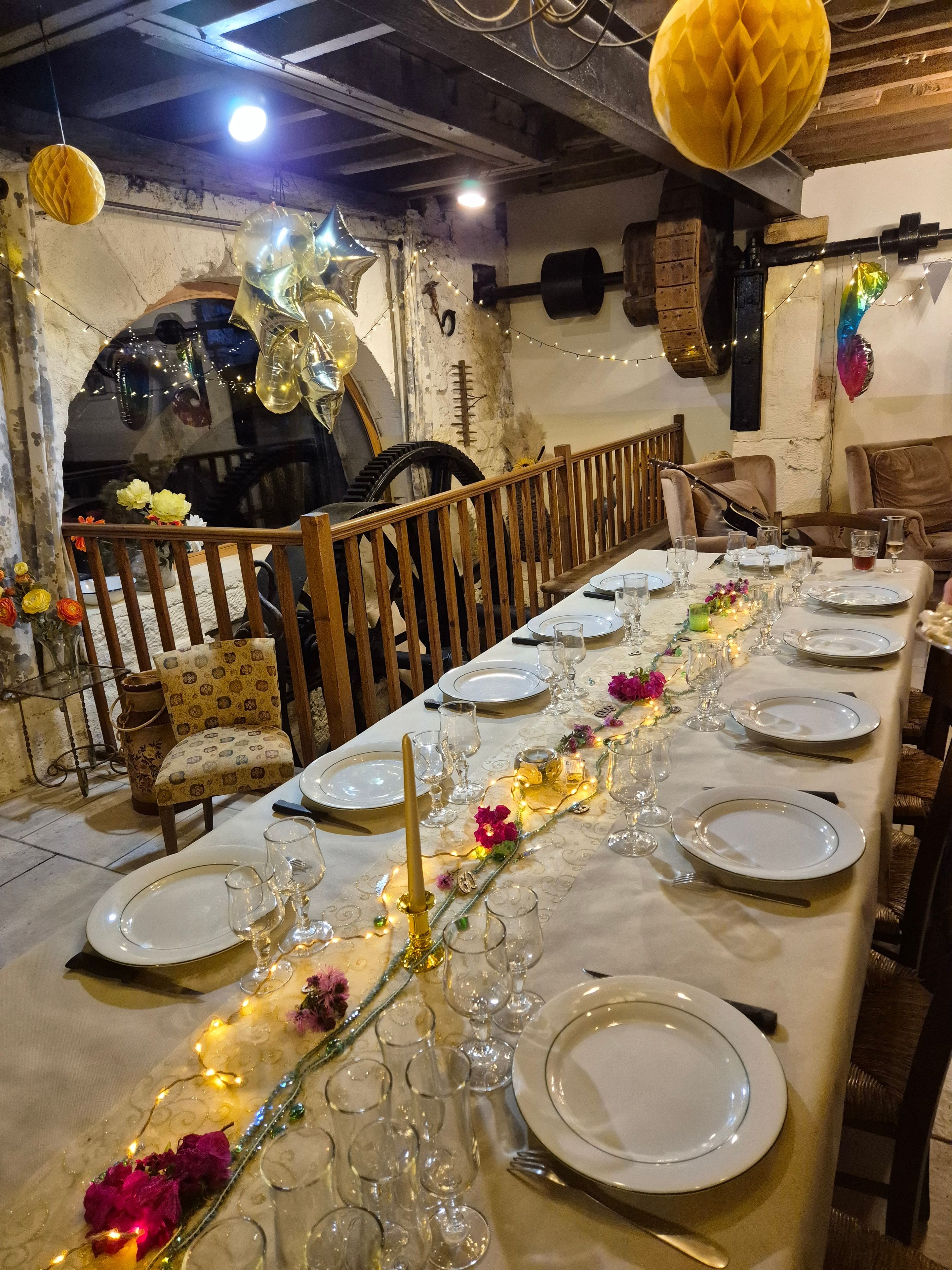 A long dining table set with plates, glasses, and cutlery, decorated with flowers and string lights.