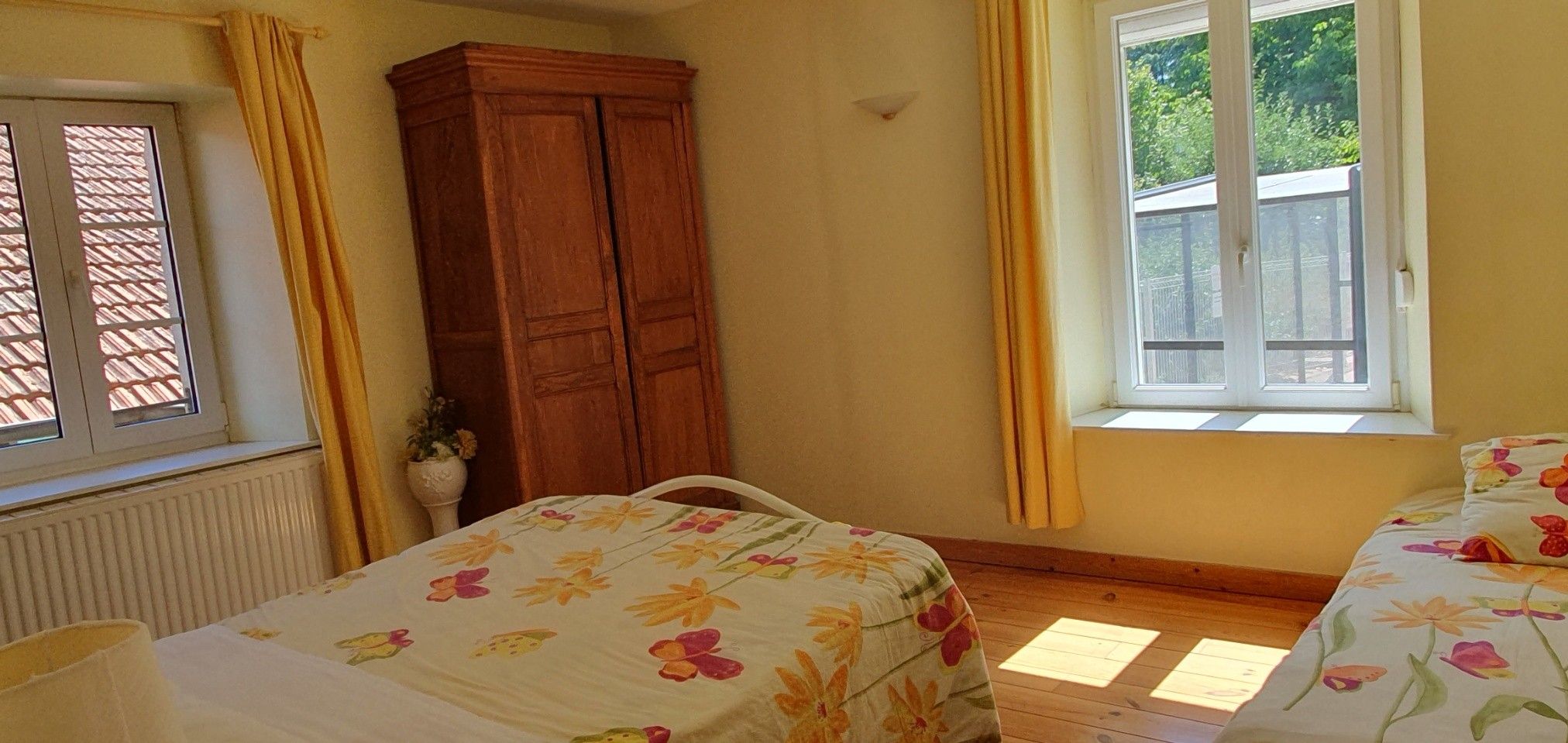 A bedroom with two beds, a wooden wardrobe, a window with curtains, and a radiator.