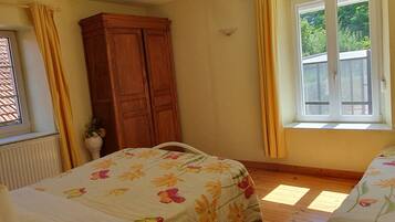 A bedroom with two beds, a wooden wardrobe, a window with curtains, and a radiator.