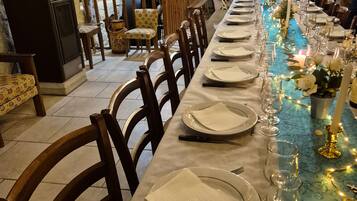 Une longue table à manger, dressée avec des assiettes, des couverts et des verres, et décorée de guirlandes lumineuses et de fleurs.
