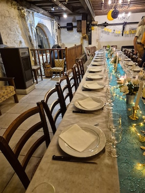A long dining table set with plates, cutlery, and glasses, decorated with string lights and flowers.