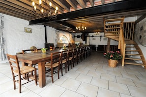 A long wooden dining table with chairs, a chandelier, and a wooden staircase.