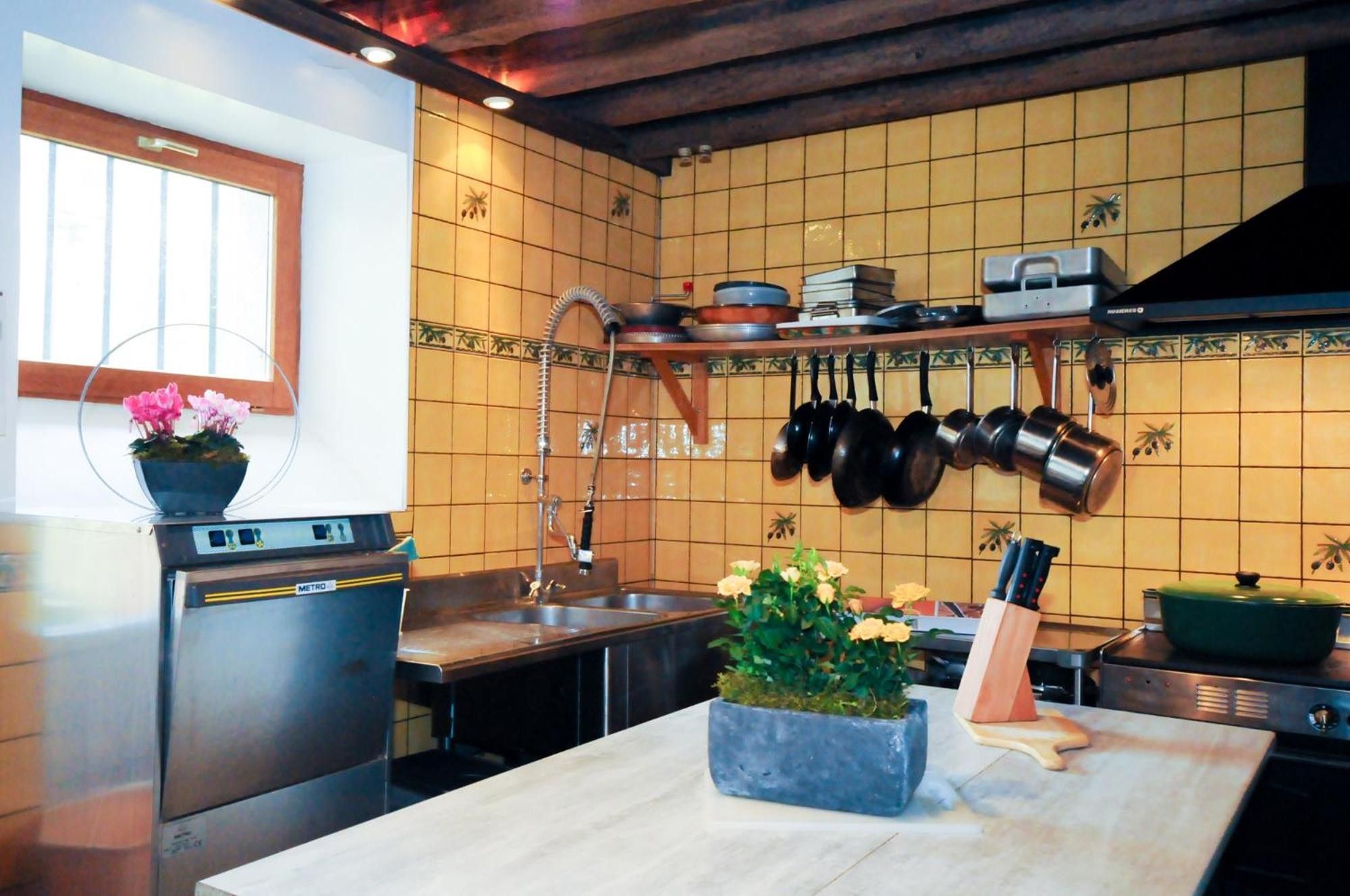 Eine Küche mit integriertem Mikrowellenherd, einer Spüle und einem Herd. Töpfe hängen an der Wand und ein Blumentopf steht auf der Arbeitsfläche.