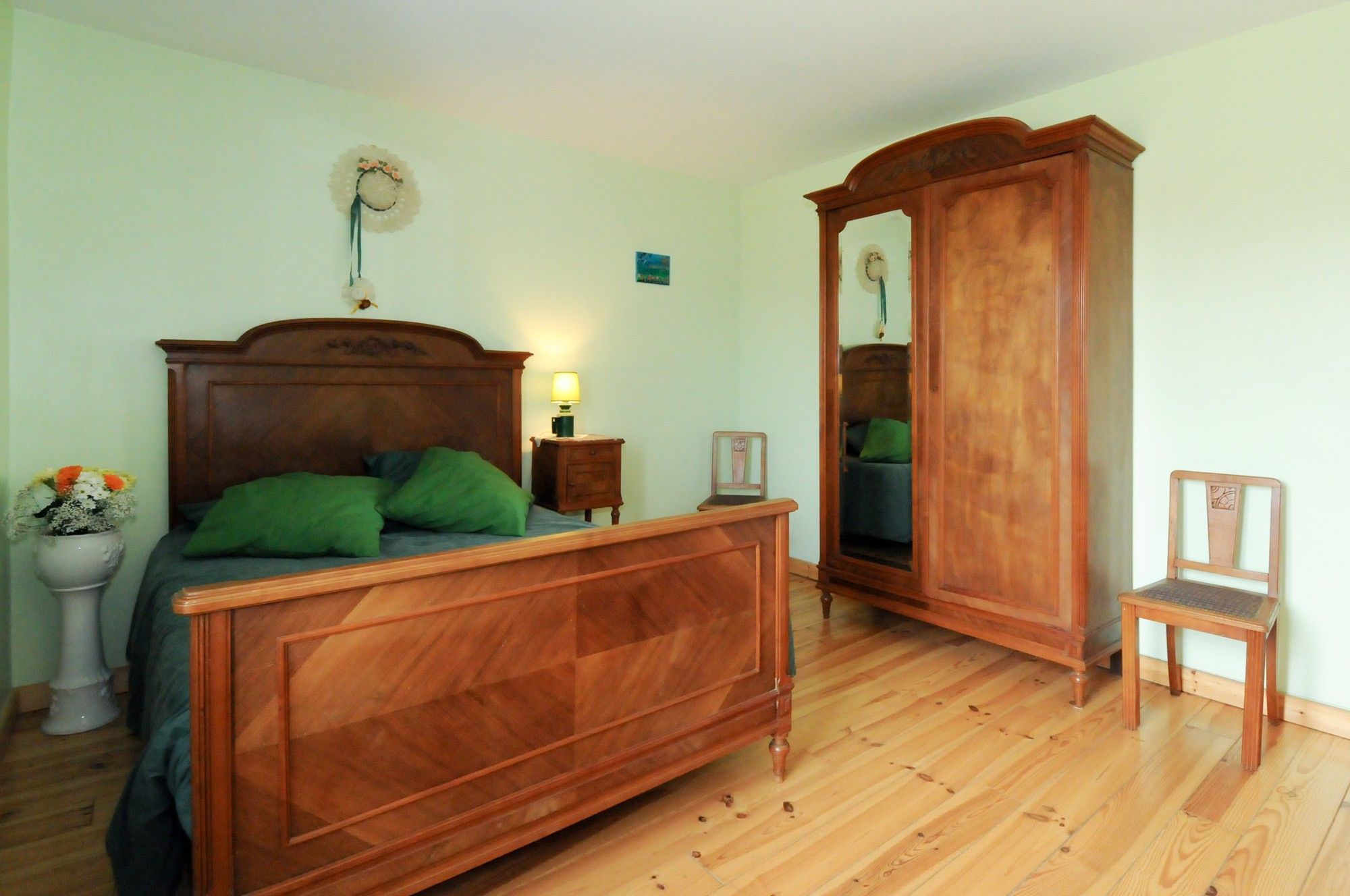 Ein Schlafzimmer mit einem hölzernen Bett, einem Nachttisch, einem Spiegel und einem Sessel.