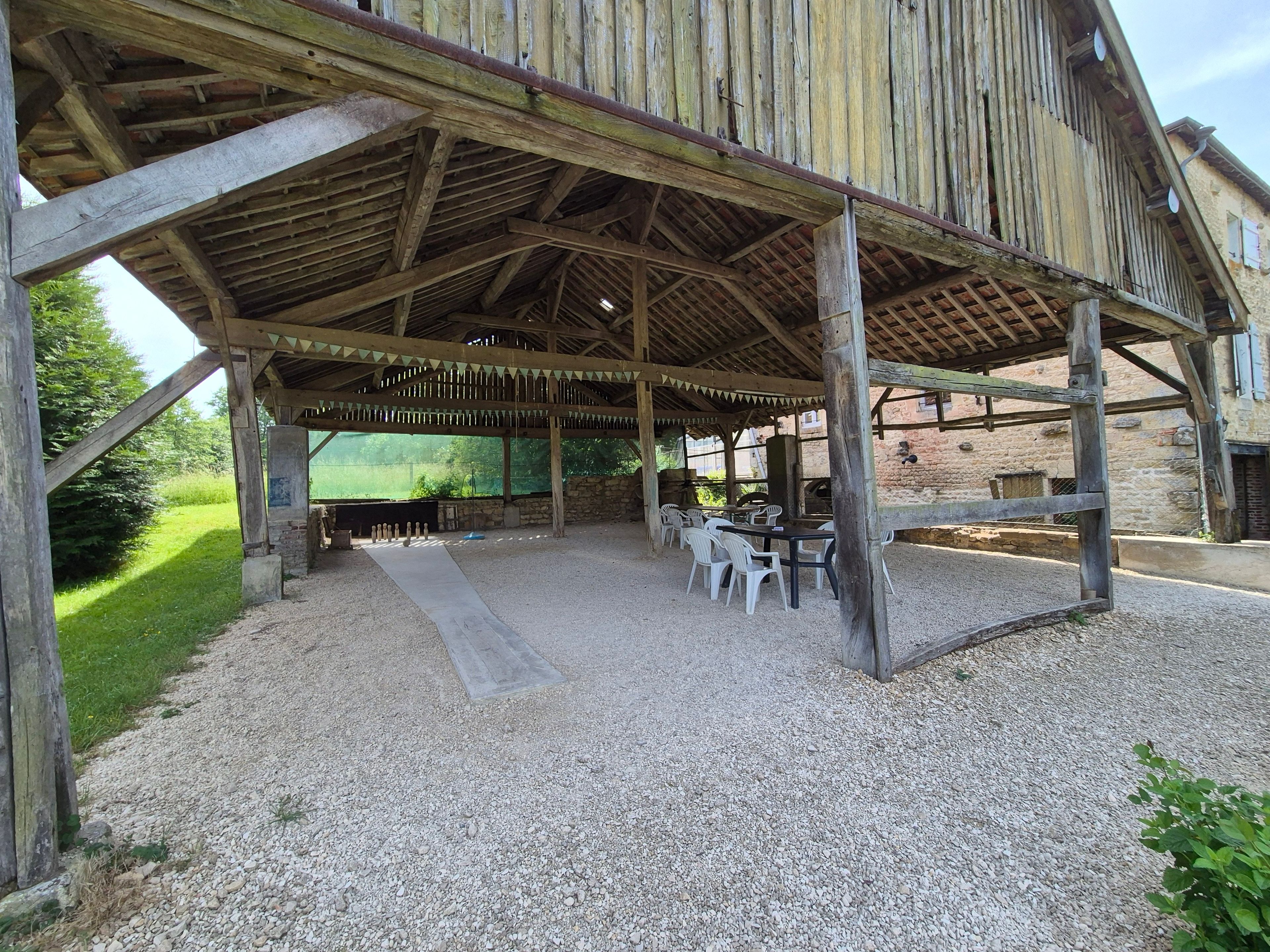 Eine überdachte Terrasse im Freien mit Tischen und Stühlen, einem Kiesboden und einer Steinwand im Hintergrund.