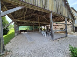 An outdoor covered patio with tables and chairs, a gravel floor, and a stone wall in the background.