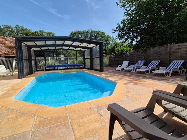 A swimming pool with a glass enclosure, surrounded by lounge chairs and a tiled patio.