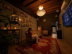 A cozy living room with a large chandelier, a red patterned rug, and a woman sitting on a floral sofa. - Siam Old Town BKK (Phra nakhon)