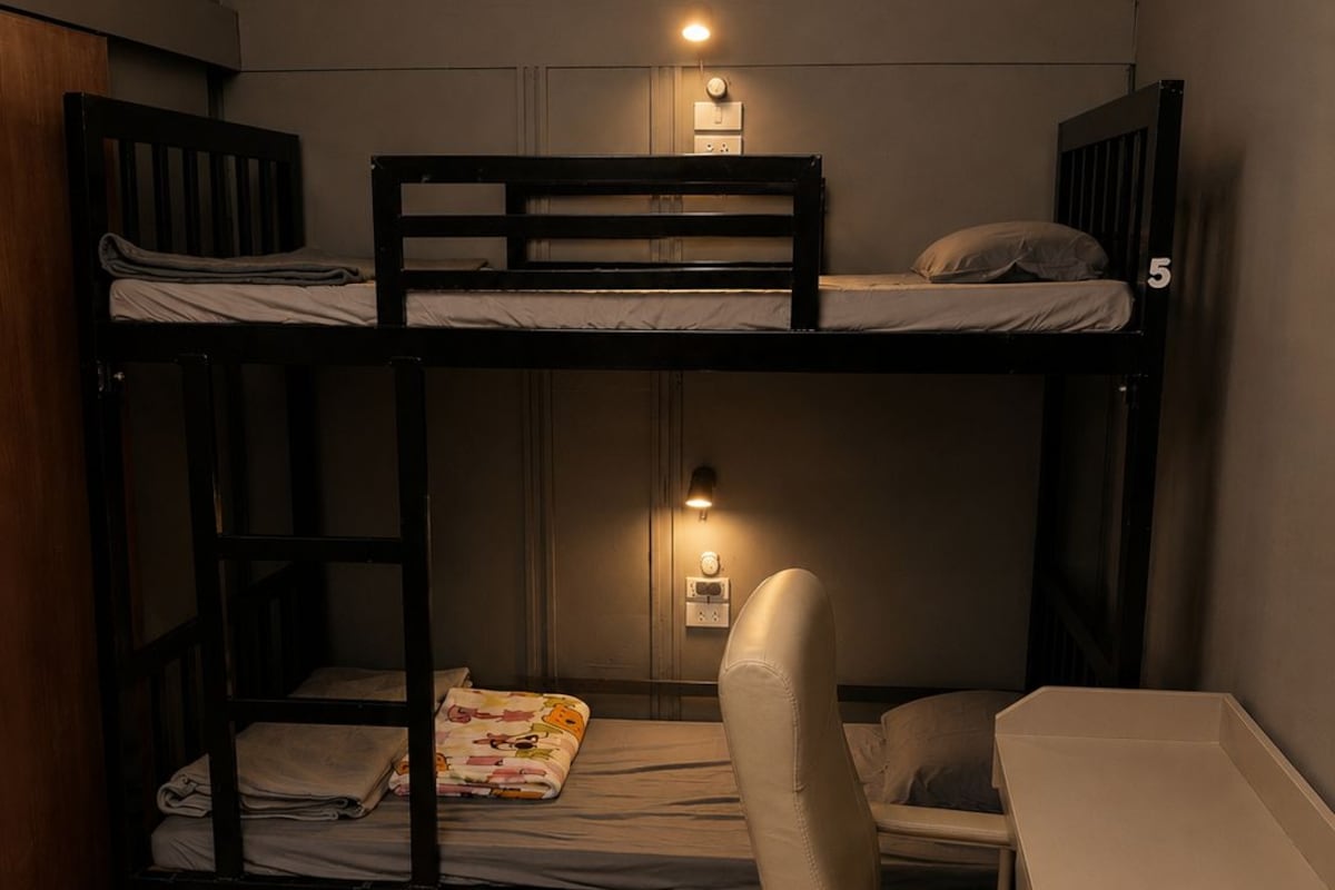 A bunk bed room with a desk and chair, a small table, and a wall socket.