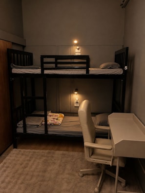 A bunk bed room with a desk and chair, a small table, and a wall socket. - Siam Old Town BKK (Phra nakhon)