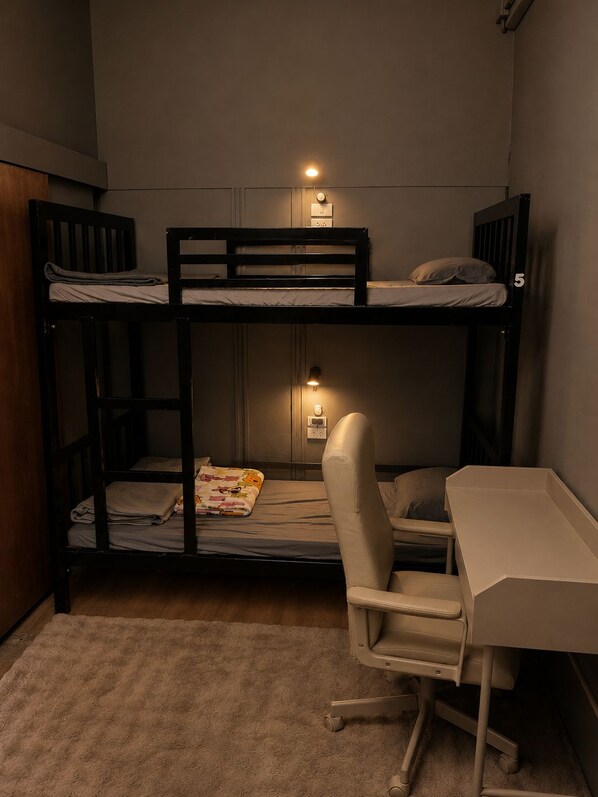 Habitación con literas, escritorio, silla, una mesita pequeña y enchufe de pared.