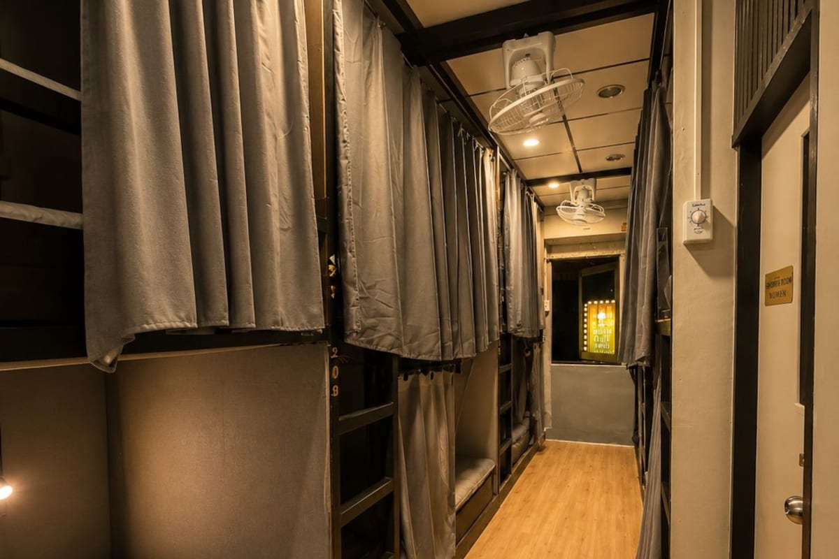 A narrow corridor with bunk beds on either side, a wooden floor, and a door at the end.