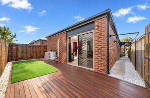Ein modernes Haus mit einer Holzterrasse, einem umzäunten Garten und einer Schiebetür zu einem Innenbereich.
