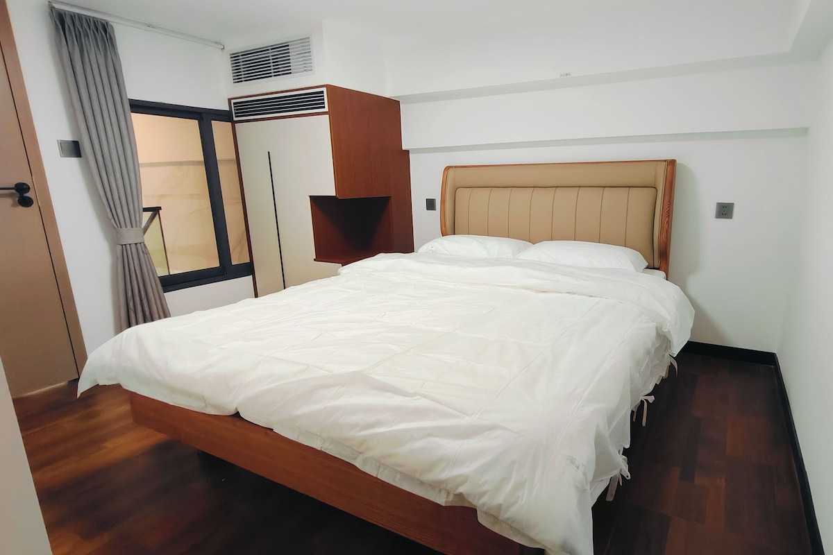 A hotel room with a bed, a wardrobe, a window with curtains, and a wall-mounted air conditioning unit.