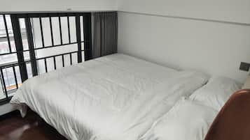 A room with a bed, a window with blinds, and a view of the street.