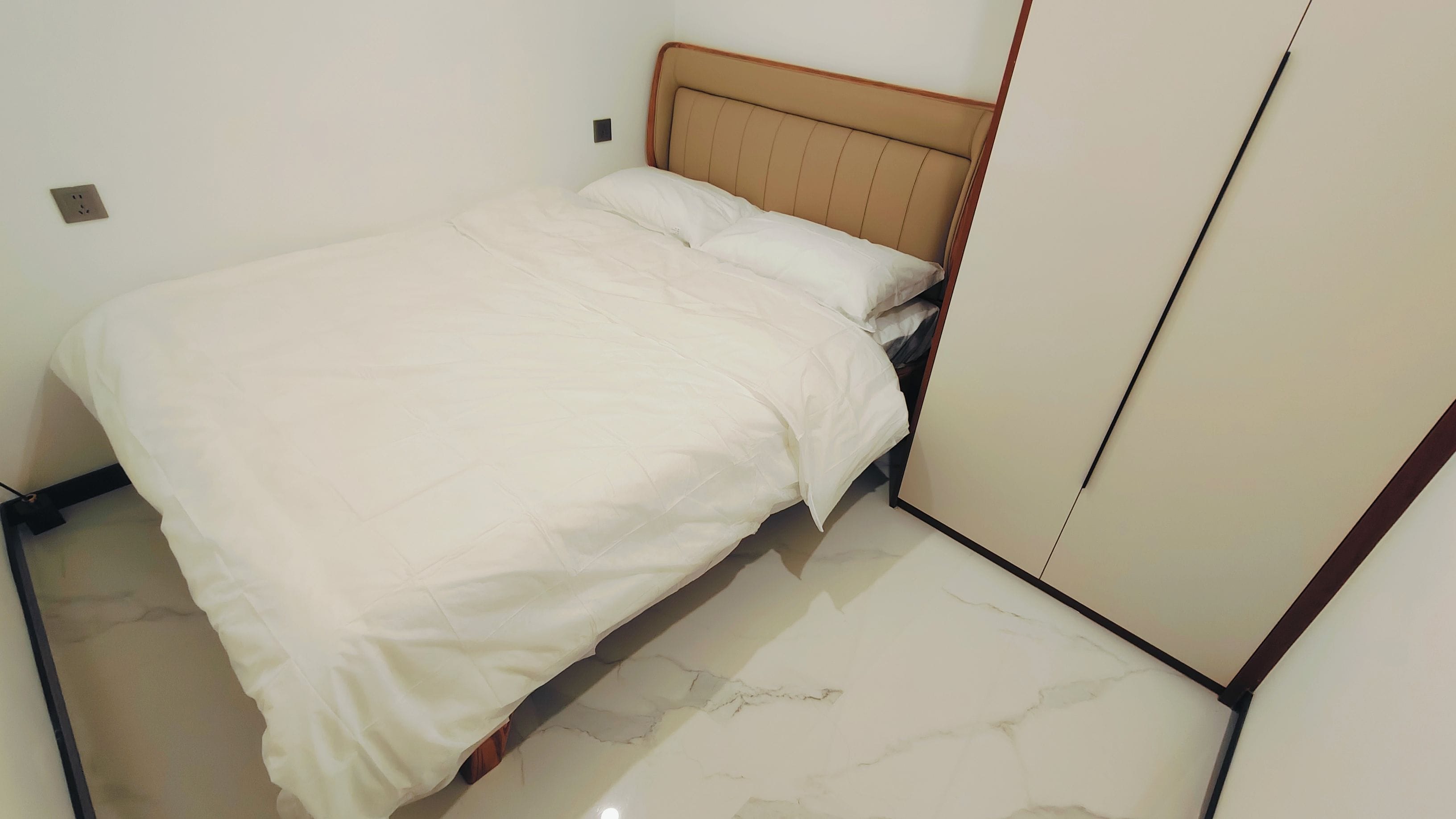 A bed with a headboard, a wardrobe, and a marble floor.