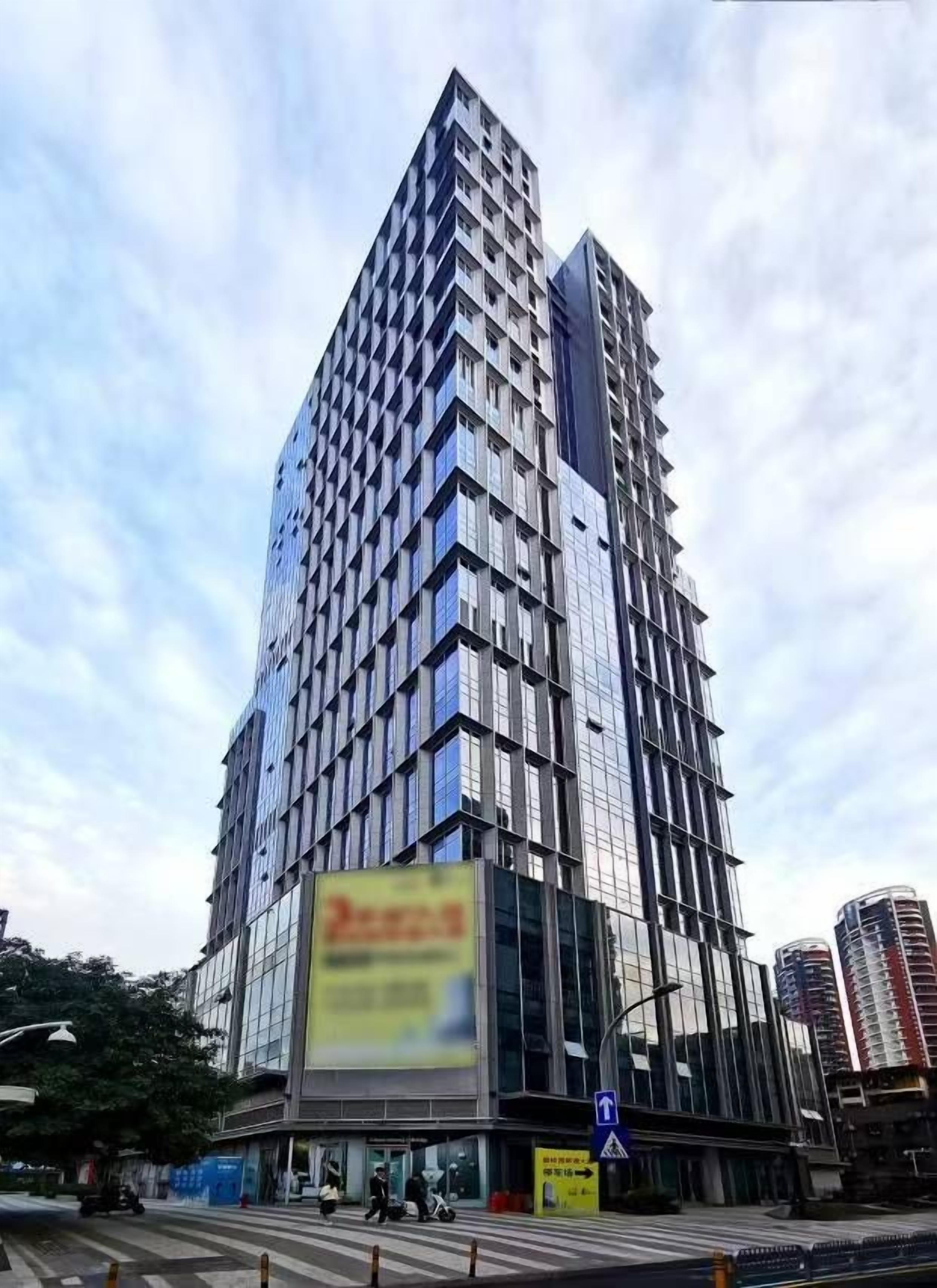 Un edificio de gran altura con un diseño arquitectónico moderno, que presenta una fachada de vidrio prominente y un gran cartel publicitario en la planta baja.