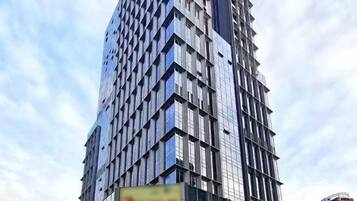 Un edificio de gran altura con un diseño arquitectónico moderno, que presenta una fachada de vidrio prominente y un gran cartel publicitario en la planta baja.