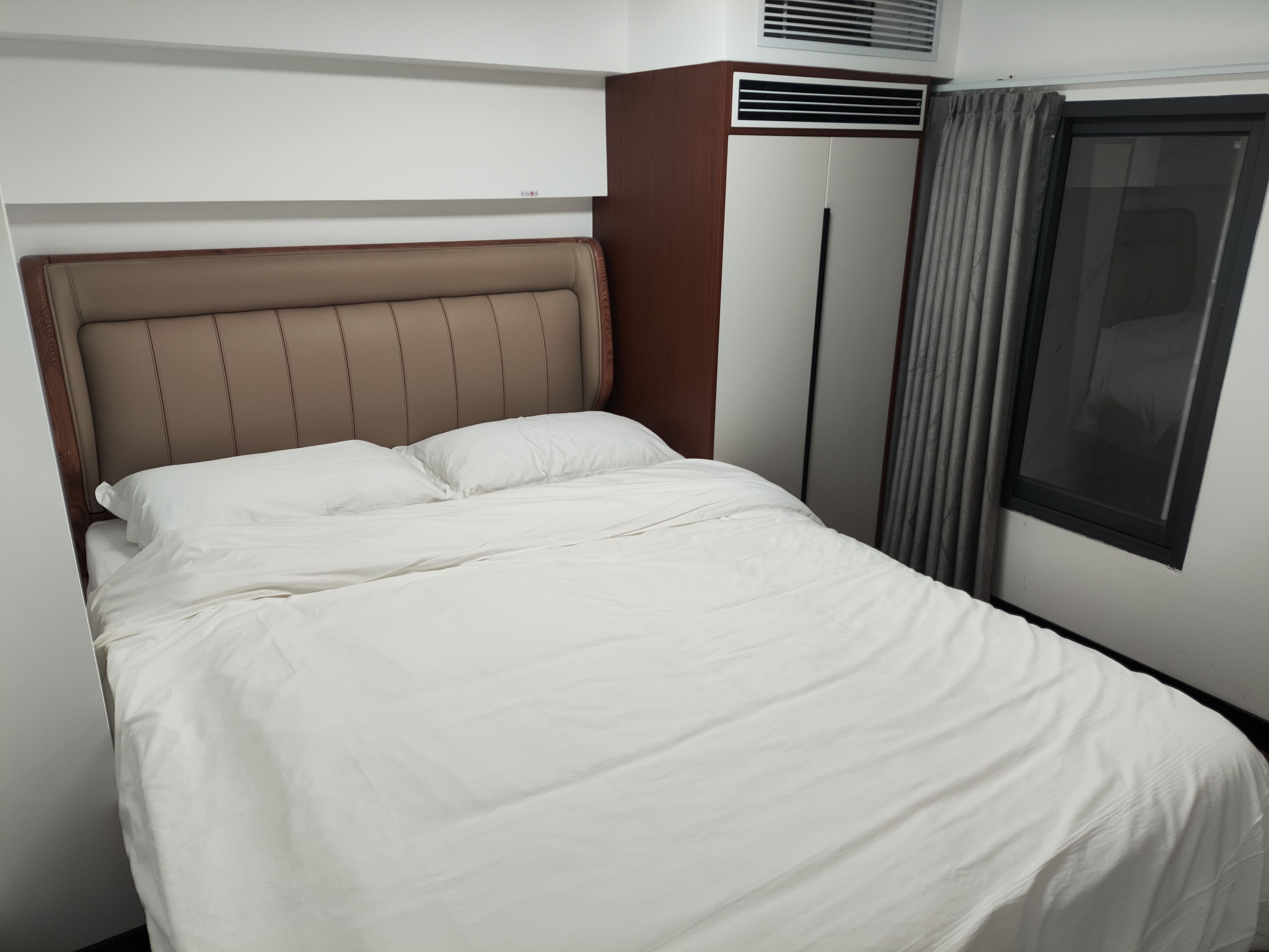 A bed with a headboard, a window with curtains, and an air conditioning unit.
