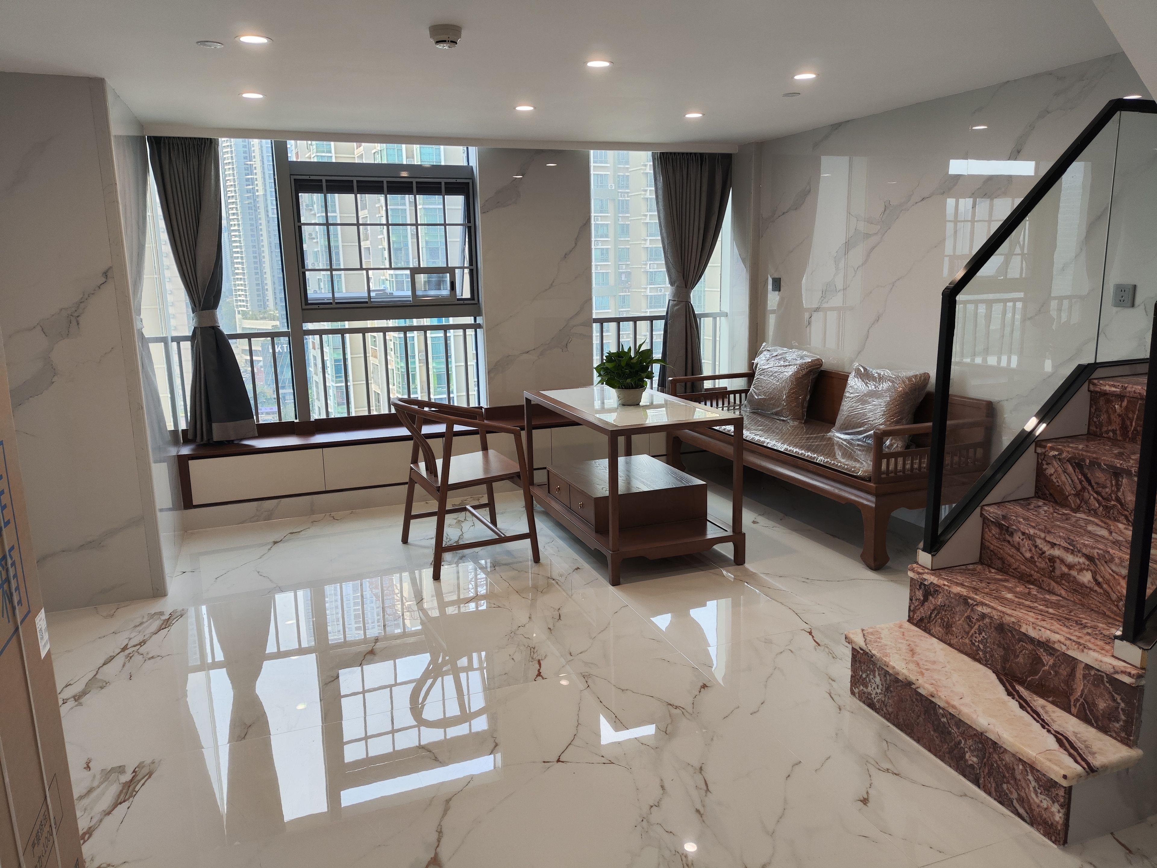 Una sala de estar moderna con piso de mármol, un sofá, una mesa de madera y una escalera.