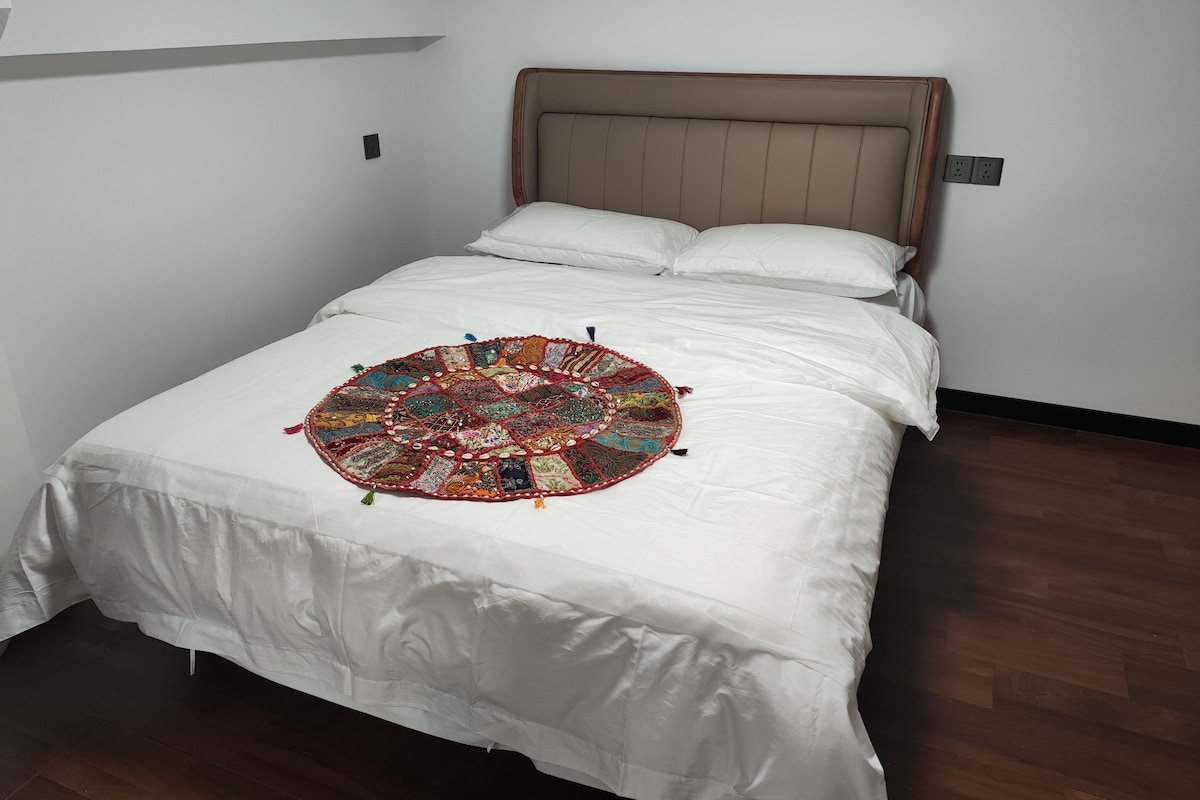 A bed with a white bedspread and a colorful, circular throw blanket.
