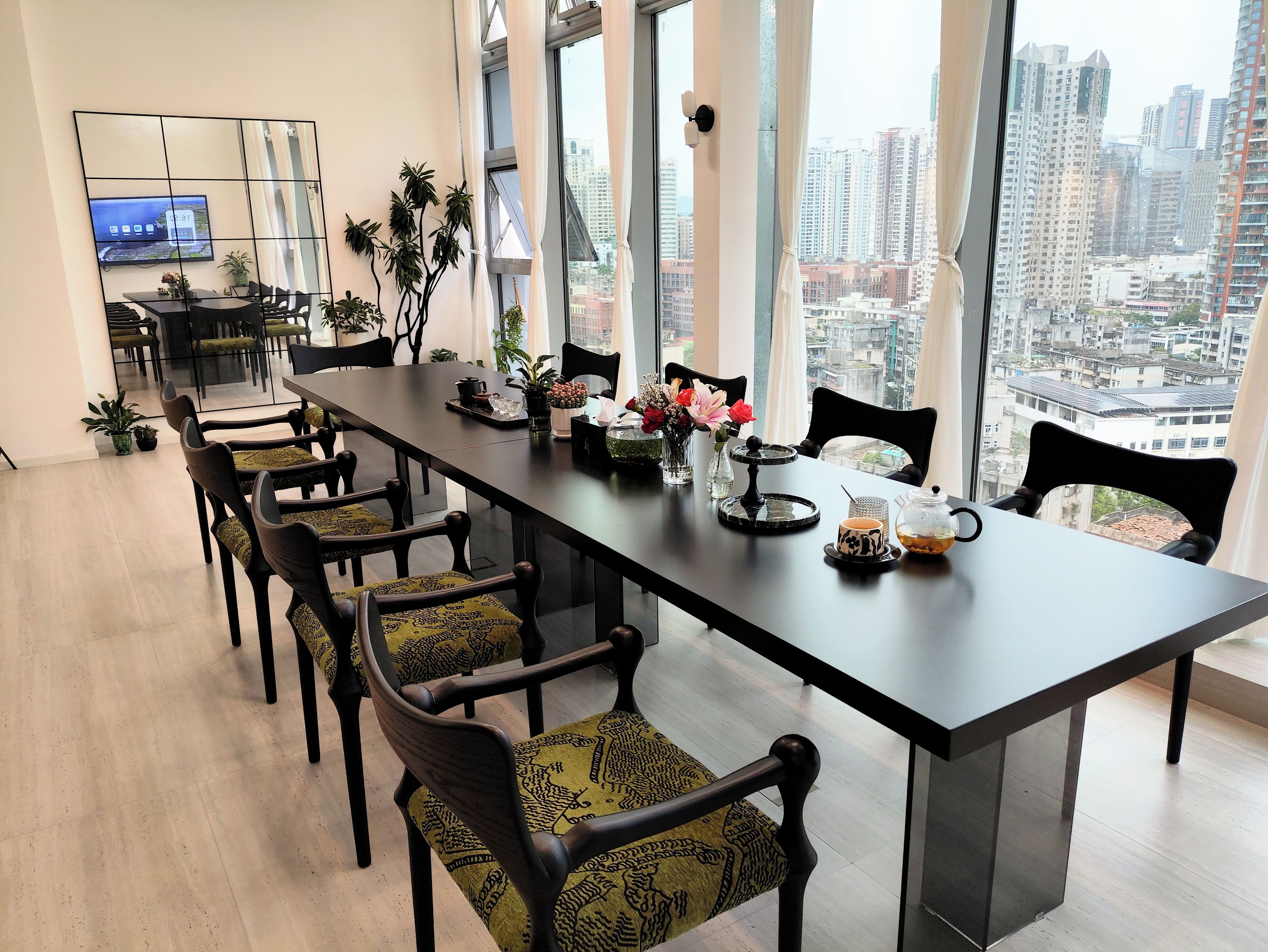 A modern conference room with a long table, chairs, and a city view through large windows.
